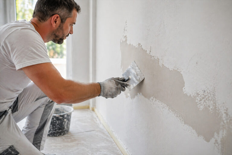 Handwerker trägt Innenputz mit Spachtel auf Wand bei Renovierungsarbeiten auf